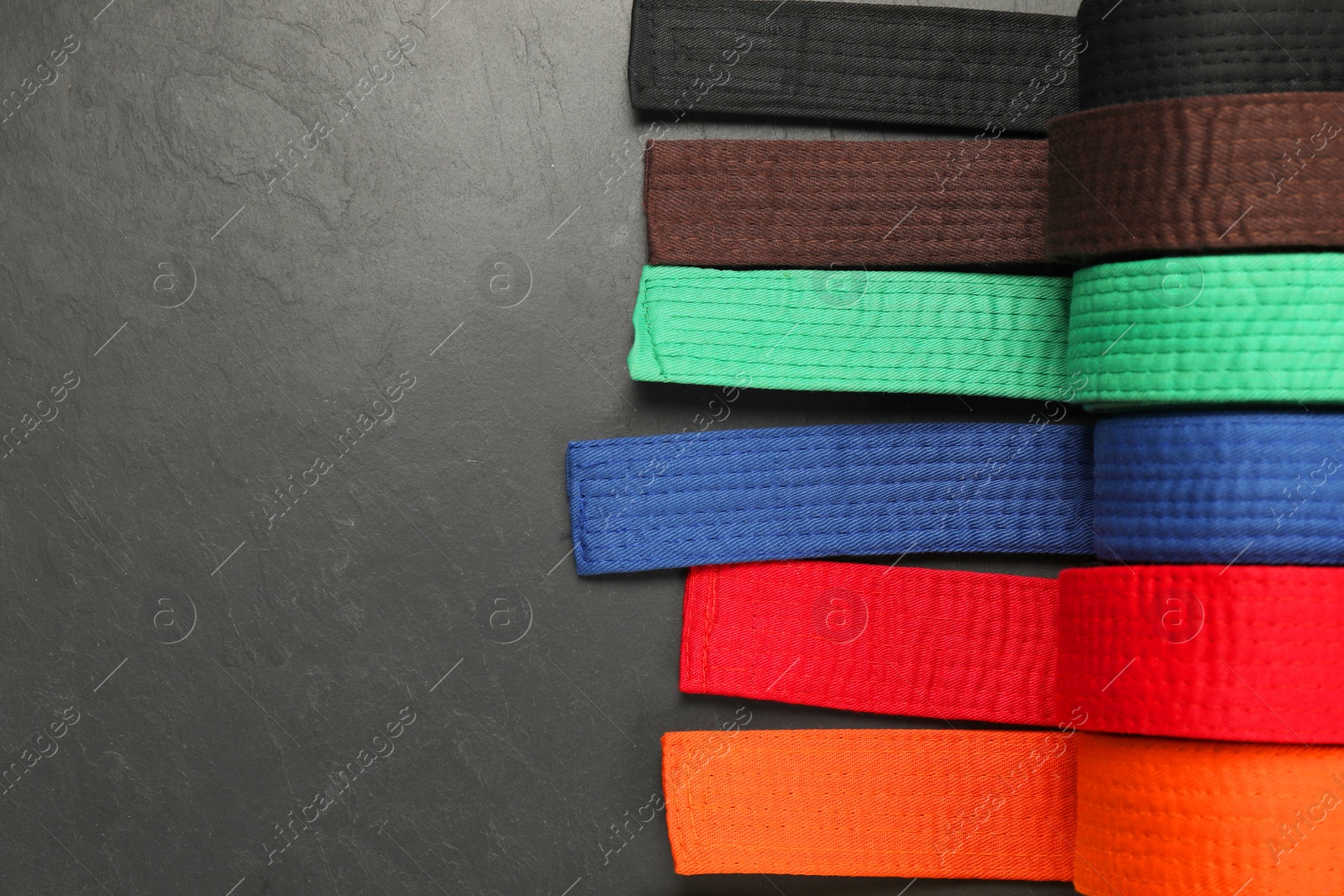 Photo of Colorful karate belts on gray background, flat lay. Space for text