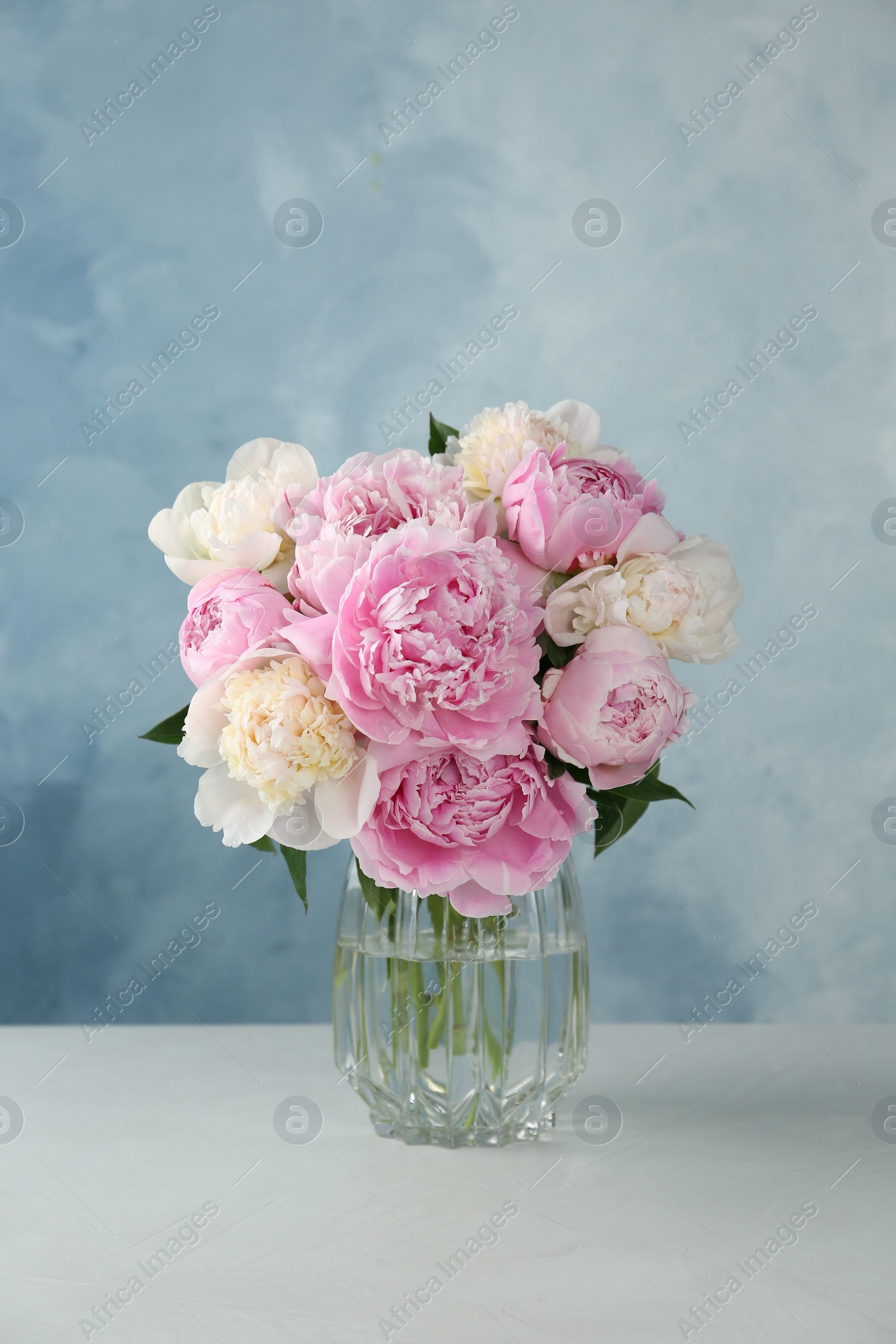 Photo of Bouquet of beautiful peonies in glass vase on white table