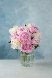 Photo of Bouquet of beautiful peonies in glass vase on white table