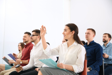 Photo of Young woman raising hand to ask question at business training indoors