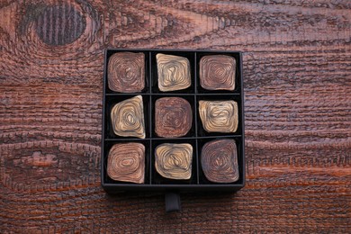 Photo of Box of tasty chocolate candies on wooden table, top view