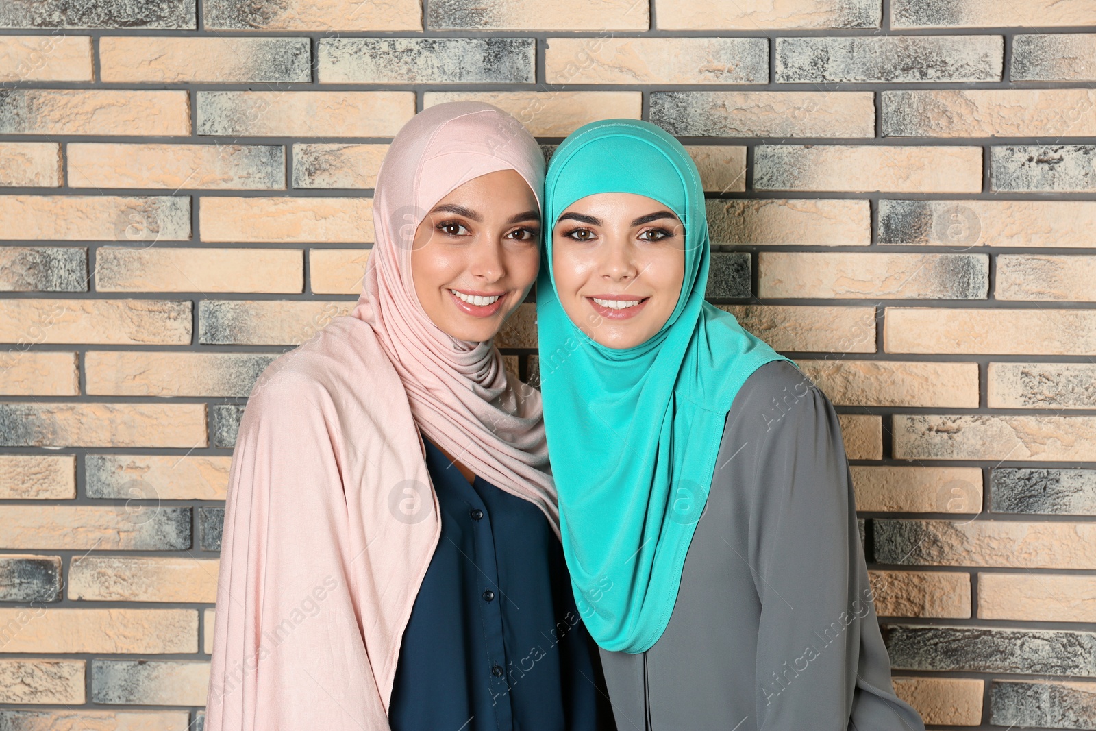 Photo of Portrait of young Muslim women in hijabs against brick wall