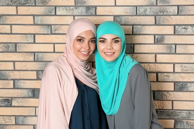 Portrait of young Muslim women in hijabs against brick wall