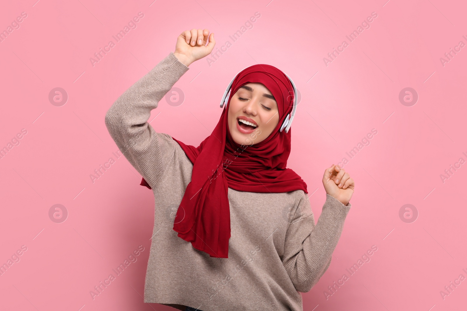 Photo of Muslim woman in hijab and headphones dancing on pink background