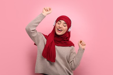 Photo of Muslim woman in hijab and headphones dancing on pink background
