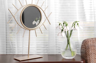 Photo of Beautiful snowdrops in vase and mirror on wooden table indoors