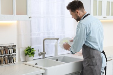 Photo of Man washing plate above sink in kitchen