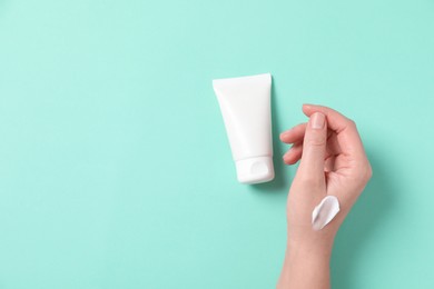 Woman with tube of hand cream on turquoise background, top view. Space for text