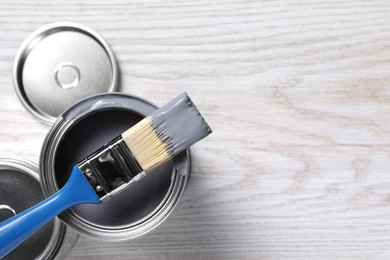 Photo of Cans of paints and brush on white wooden table, flat lay. Space for text