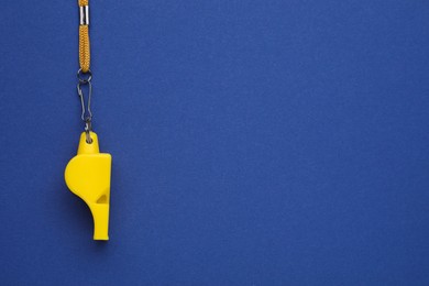 Photo of One yellow whistle with cord on blue background, top view. Space for text