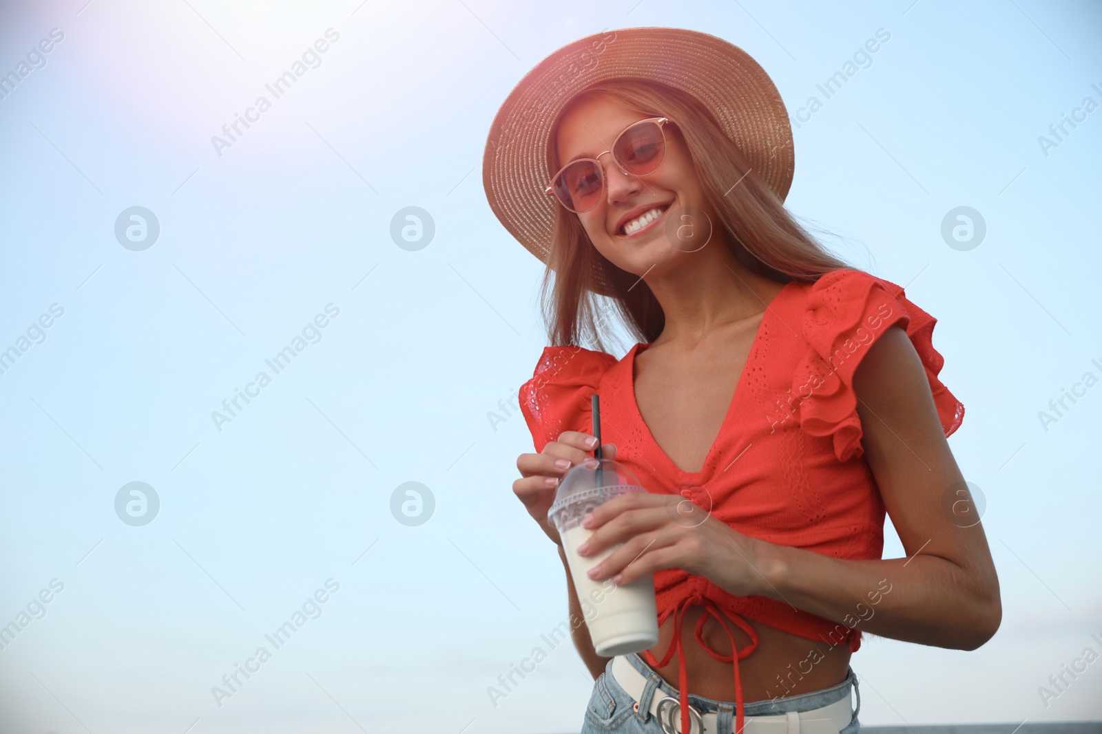 Photo of Beautiful young woman with tasty milk shake outdoors, space for text