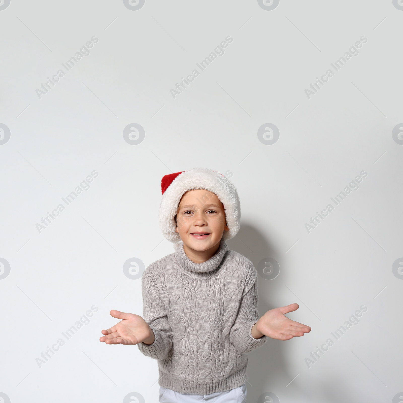 Photo of Cute little boy in warm sweater and Christmas hat on white background