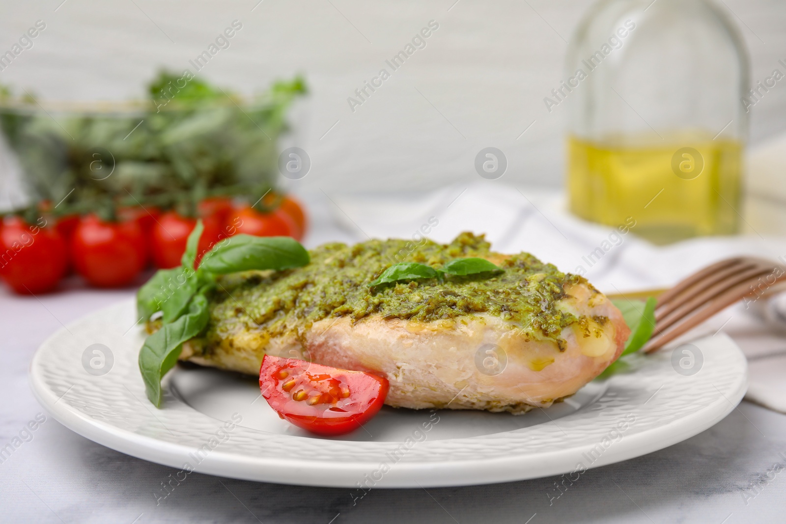 Photo of Delicious chicken breast with pesto sauce, tomato and basil on white table, closeup