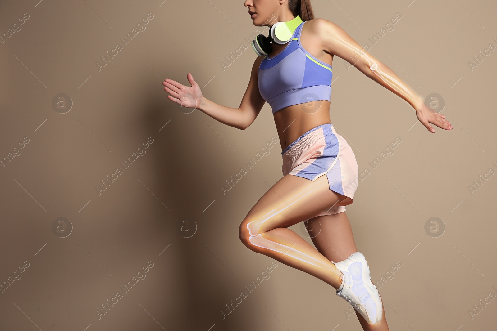 Image of Digital compositehighlighted bones and woman in sportswear with headphones running on beige background