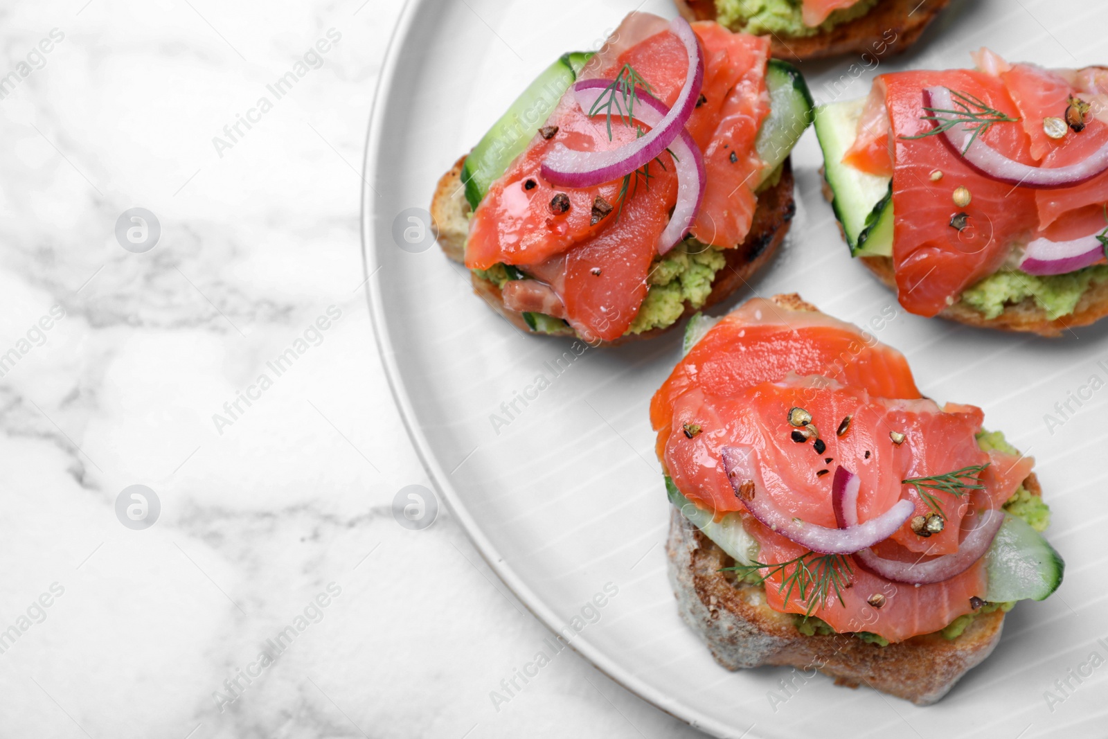 Photo of Delicious sandwiches with salmon, avocado, cucumber and onion on white marble table, top view. Space for text