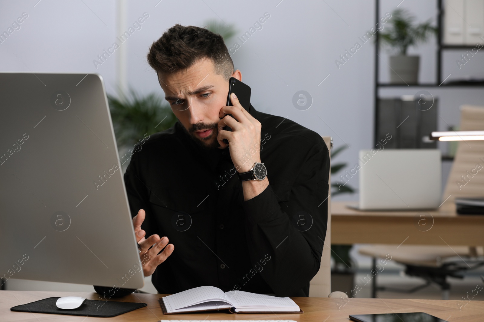 Photo of Man talking on phone while working at table in office