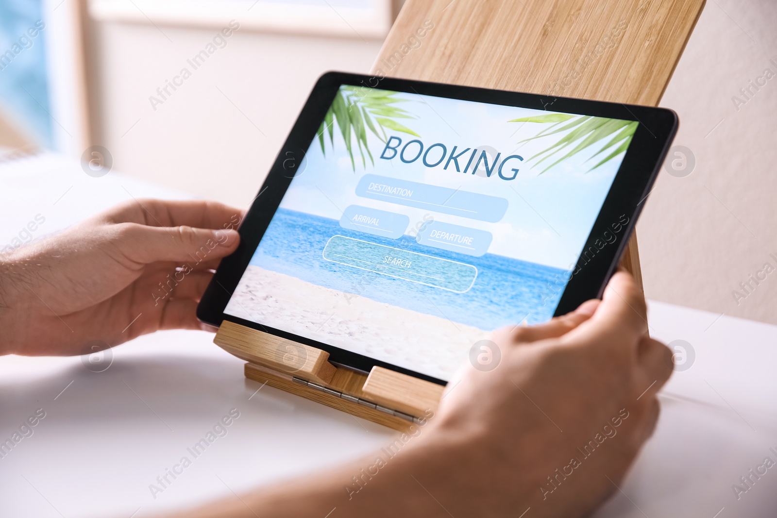 Photo of Man booking tickets online on tablet at white table, closeup. Travel agency concept