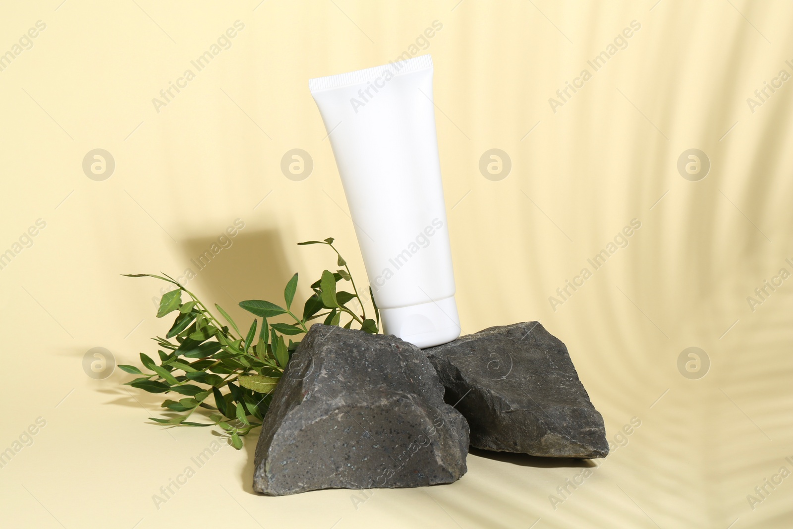 Photo of Tube of cream, branches and stones on light yellow background