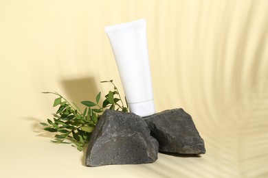 Tube of cream, branches and stones on light yellow background