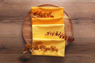 Photo of Tray with different kitchen napkins and decorative dry leaves on wooden table, top view