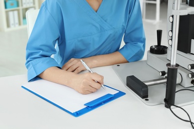 Photo of Ophthalmologist with modern equipment and clipboard in clinic