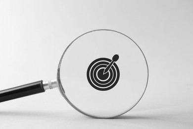Target with dart on white background, view through magnifying glass