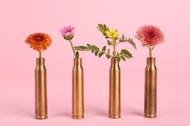 Photo of Bullet cartridge cases and beautiful flowers on pink background