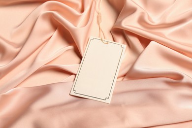Photo of Blank white tag on light pink silky fabric. Space for text