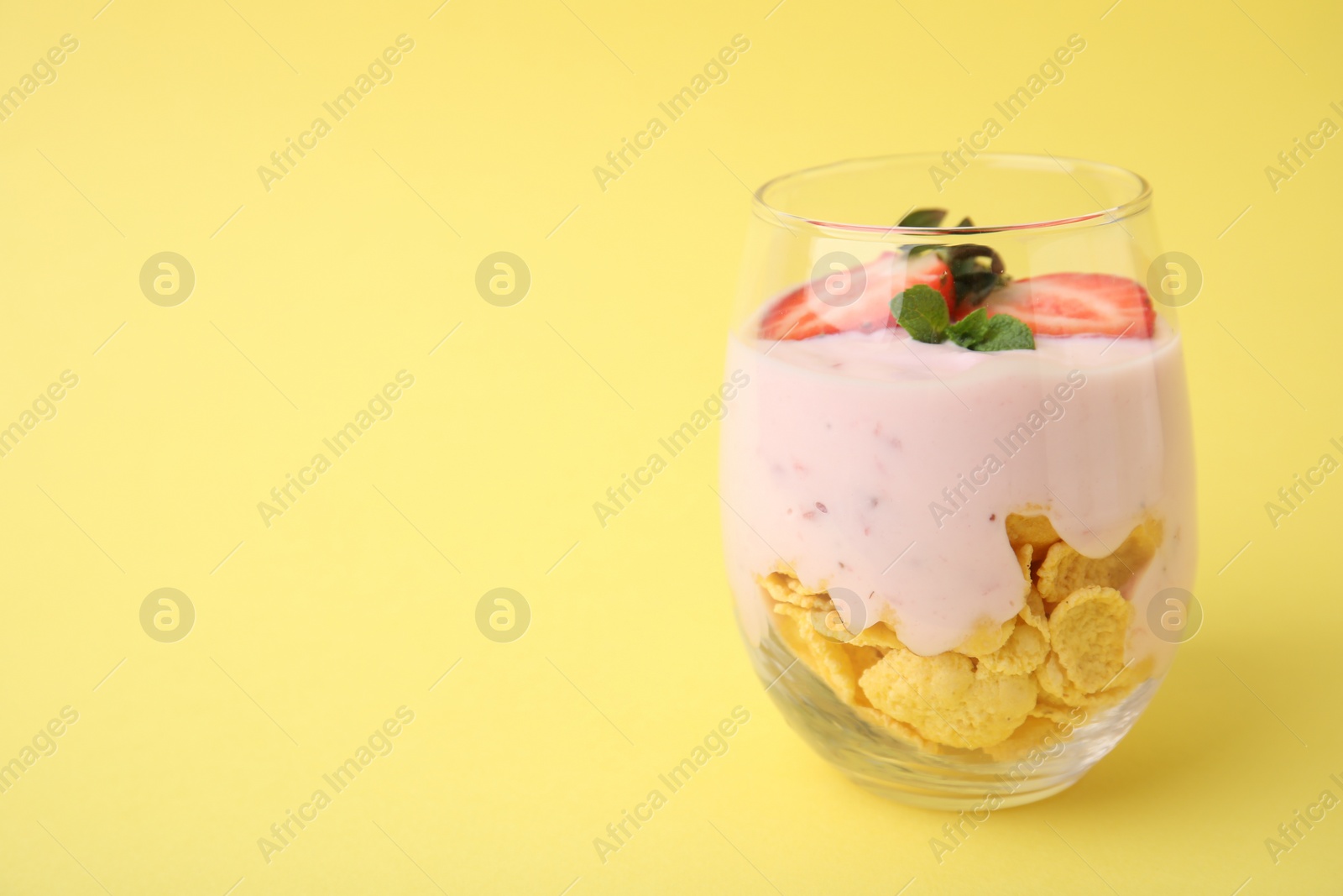 Photo of Glass with yogurt, strawberries and corn flakes on yellow background. Space for text
