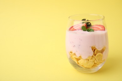 Glass with yogurt, strawberries and corn flakes on yellow background. Space for text