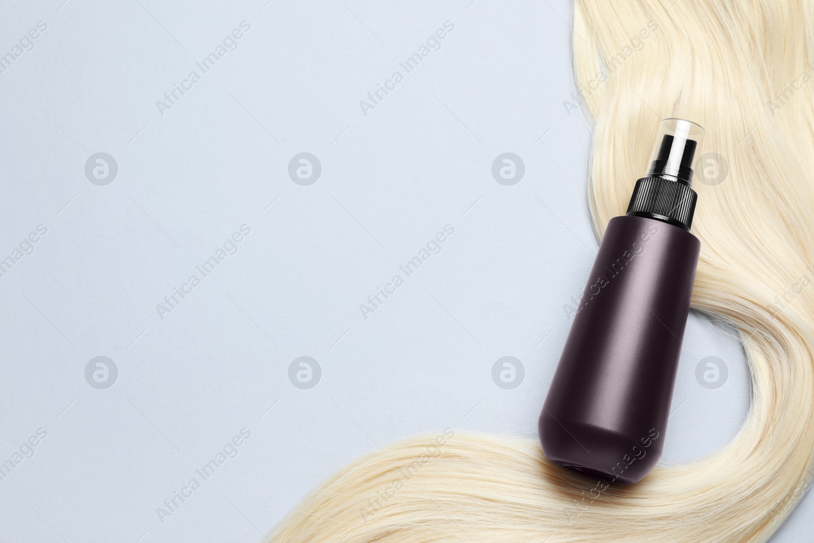 Photo of Spray bottle with thermal protection and lock of blonde hair on light background, flat lay. Space for text