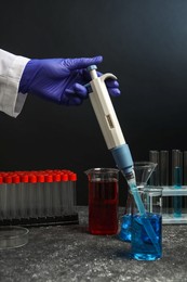 Photo of Laboratory analysis. Scientist dripping sample with micropipette into beaker at grey table, closeup