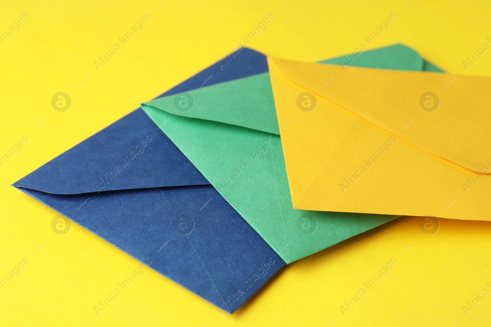 Photo of Colorful paper envelopes on yellow background, closeup