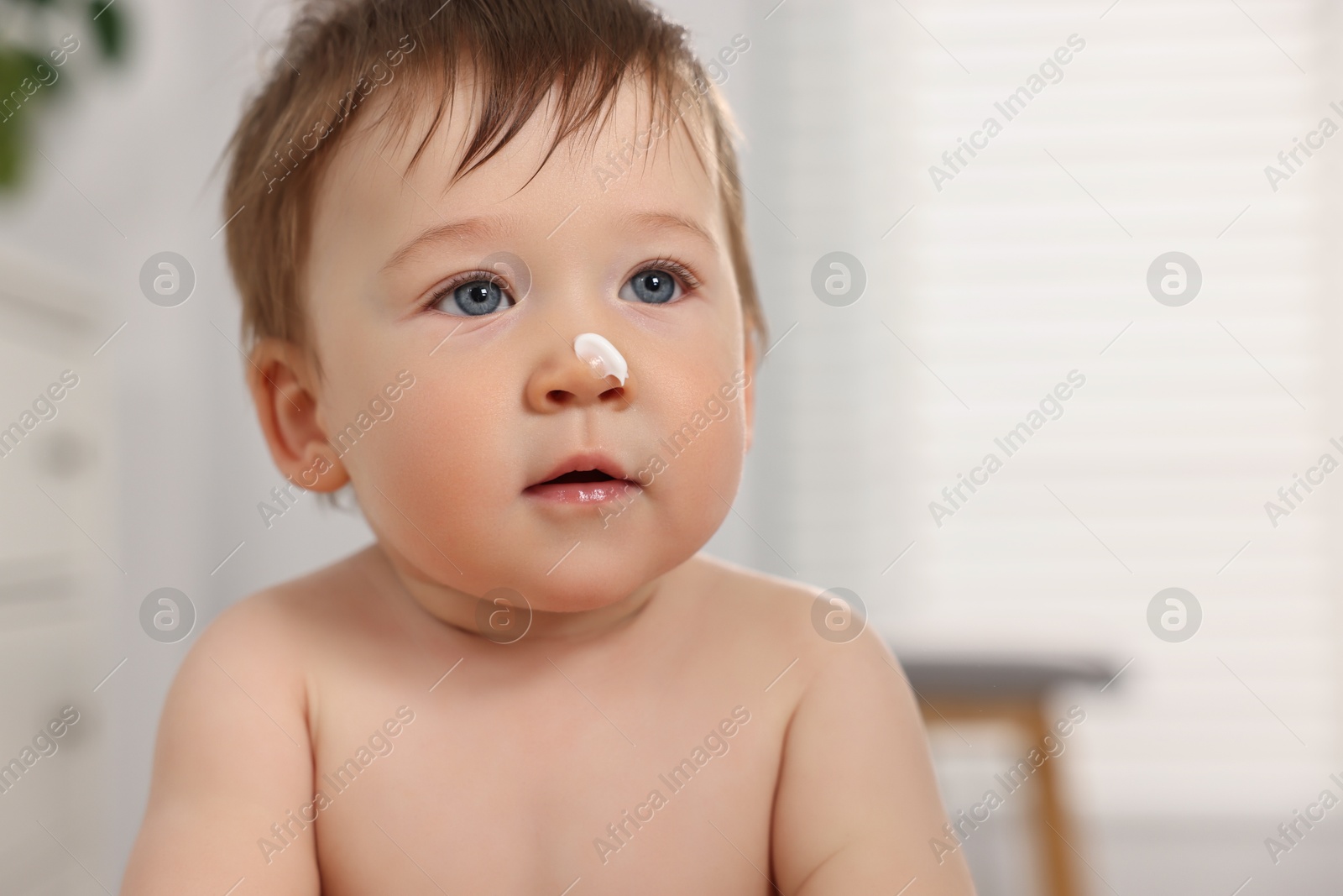 Photo of Cute little baby with moisturizing cream on face indoors