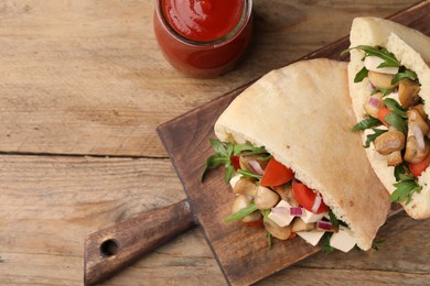 Delicious pita sandwiches with cheese, mushrooms, tomatoes and arugula on wooden table, flat lay. Space for text