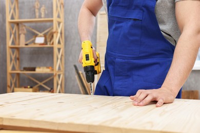 Photo of Young worker using electric drill at table in workshop, closeup