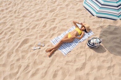 Woman resting under striped beach umbrella at sandy coast