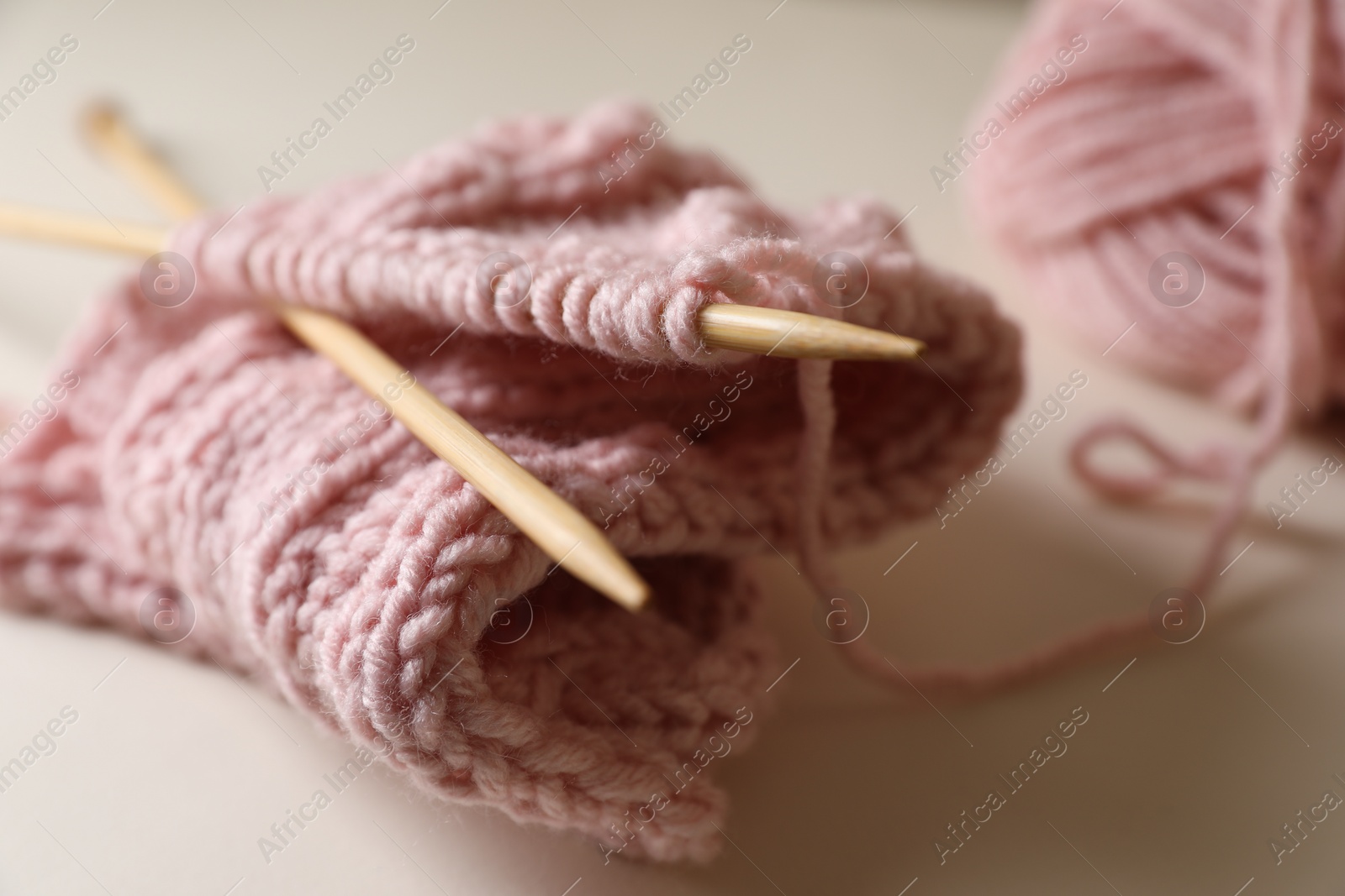 Photo of Pink knitting and needles on beige background, closeup