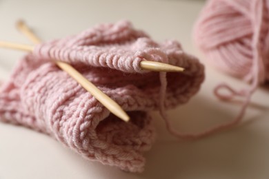 Pink knitting and needles on beige background, closeup