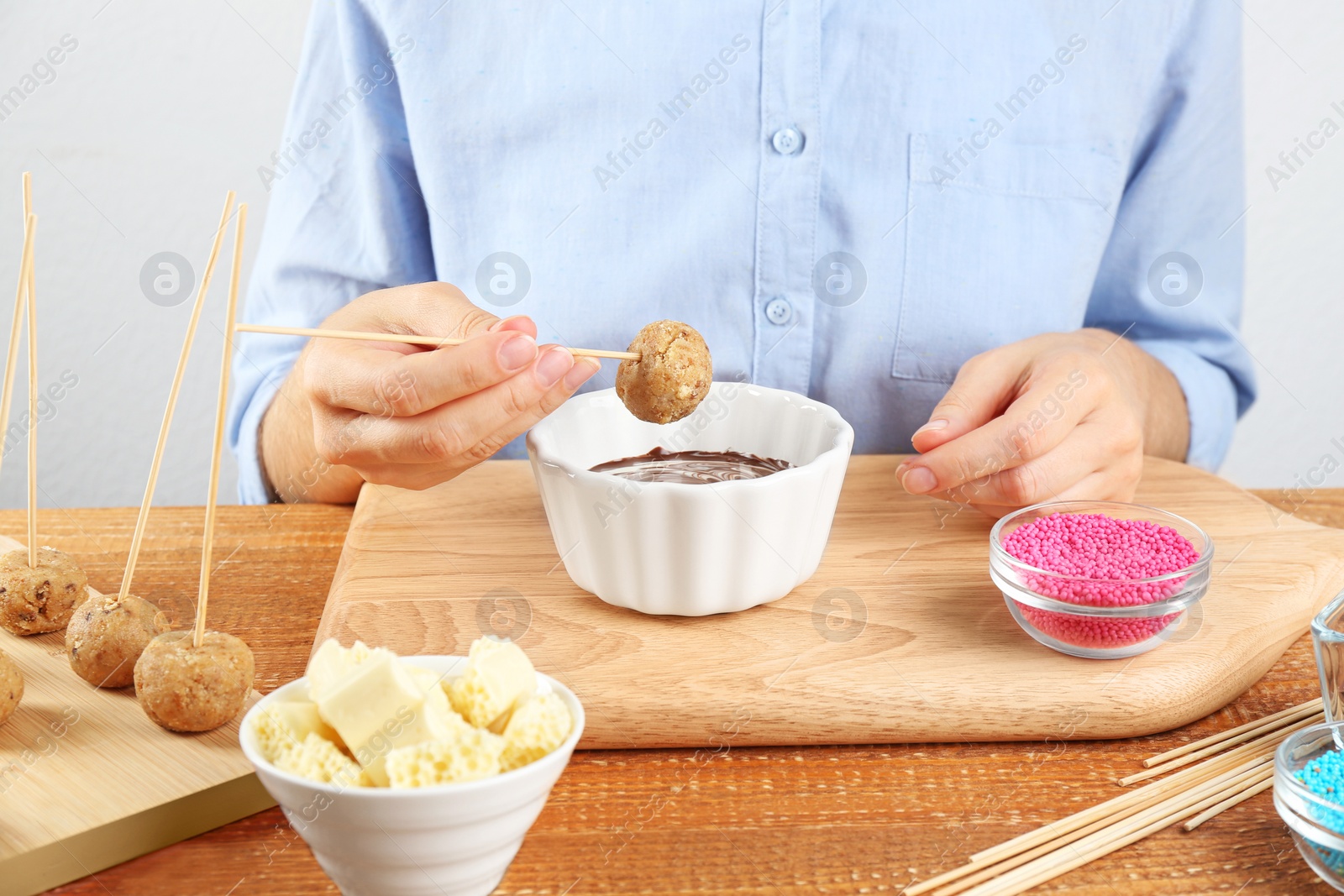 Photo of Young woman with cake pop and chocolate frosting at wooden table, closeup