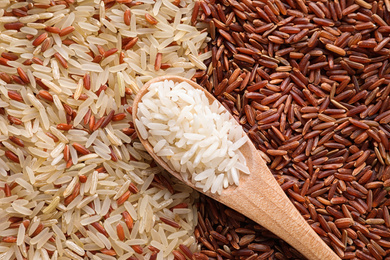 Different types of rice with wooden spoon, top view