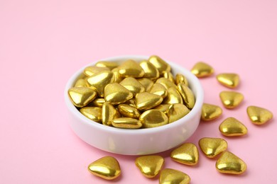Photo of Bowl and delicious heart shaped candies on pink background