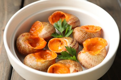 Delicious cooked snails with parsley in bowl on table, closeup