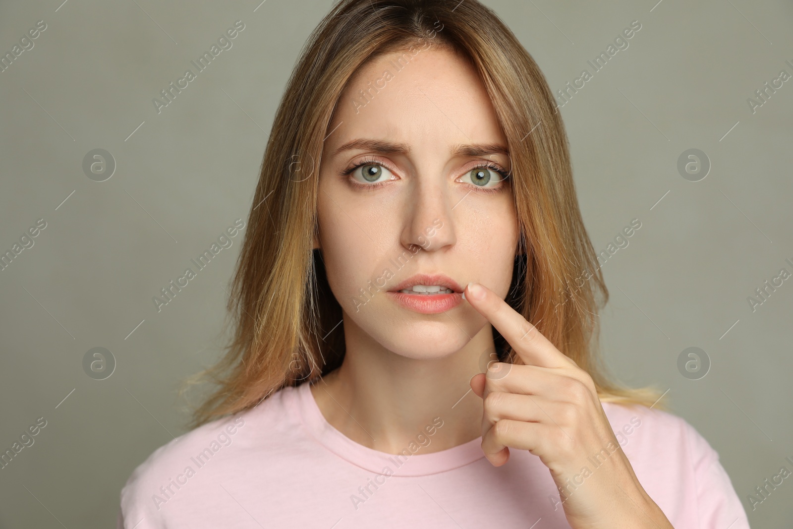 Photo of Woman with herpes applying cream onto lip against  light grey background