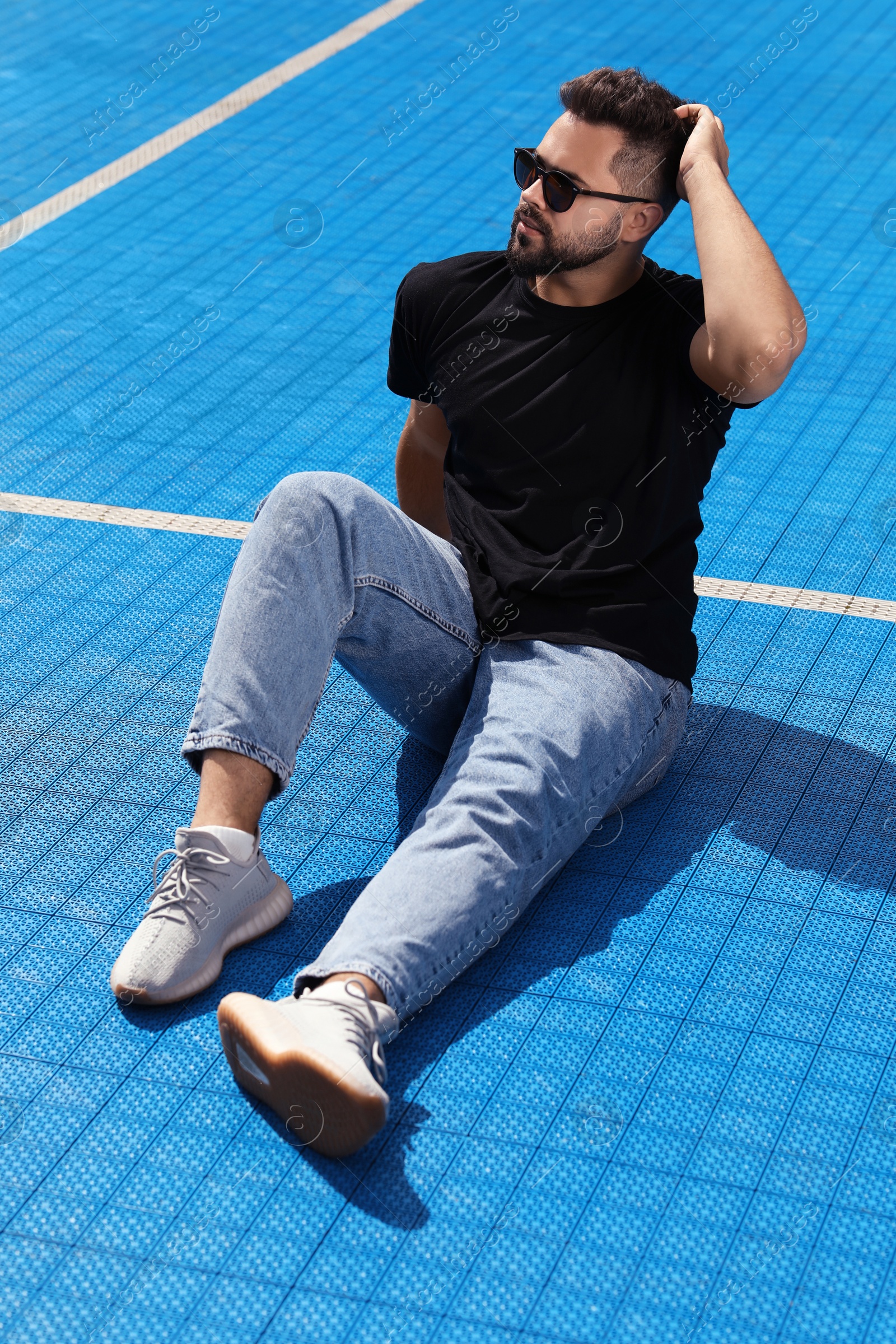 Photo of Handsome man in sunglasses on blue floor covering outdoors