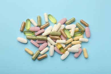 Different vitamin pills on light blue background, flat lay
