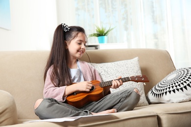 Cute little girl playing guitar on sofa in room