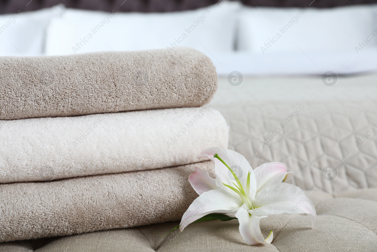 Photo of Stack of fresh towels with flower on soft bench in bedroom. Space for text