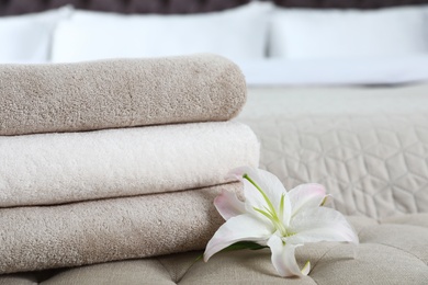 Stack of fresh towels with flower on soft bench in bedroom. Space for text