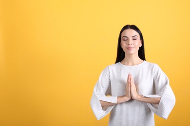 Photo of Young woman meditating on yellow background, space for text. Stress relief exercise
